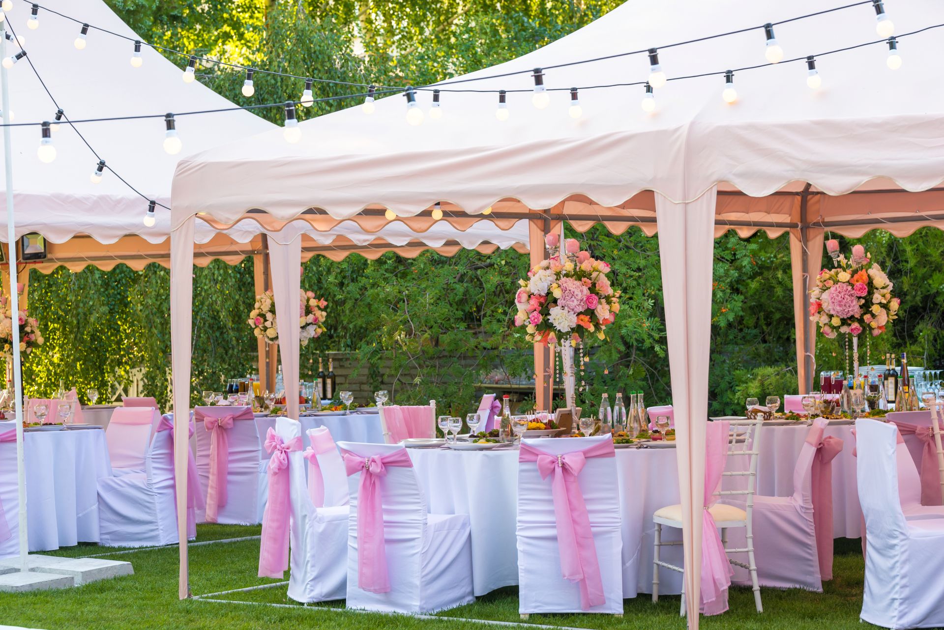 Pavillon im Garten, festlich dekoriert mit rosa Schleifen, Blumengestecken und Lichterkette für eine Sommerfeier